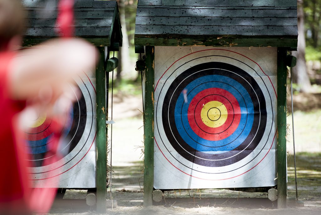 A selective focus shot of a target with a blurred person using bow and arrow